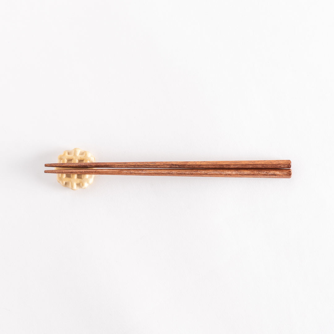 Waffle-shaped ceramic chopsticks rest with wooden chopsticks resting across it.