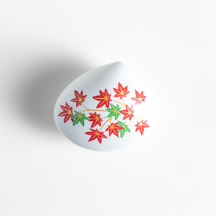 White ceramic incense holder shaped like a seashell, adorned with red and green maple leaves, featuring a small red incense stand inside for secure placement.