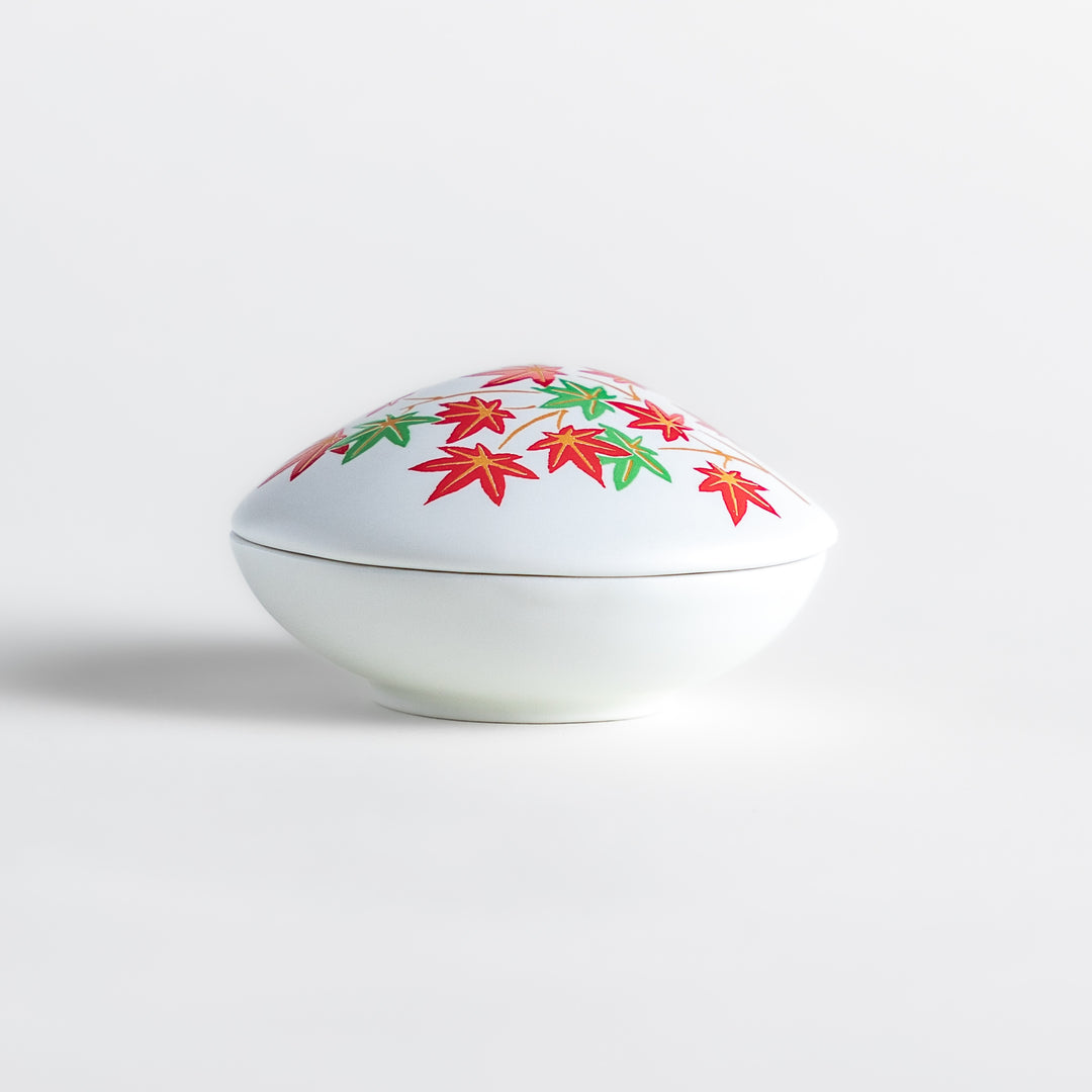 White ceramic incense holder shaped like a seashell, adorned with red and green maple leaves, featuring a small red incense stand inside for secure placement.