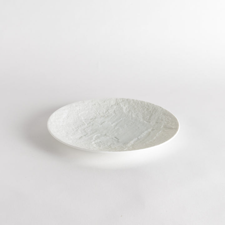 A white luncheon plate featuring a slightly irregular, organic texture and shape, providing a minimalist and natural look.