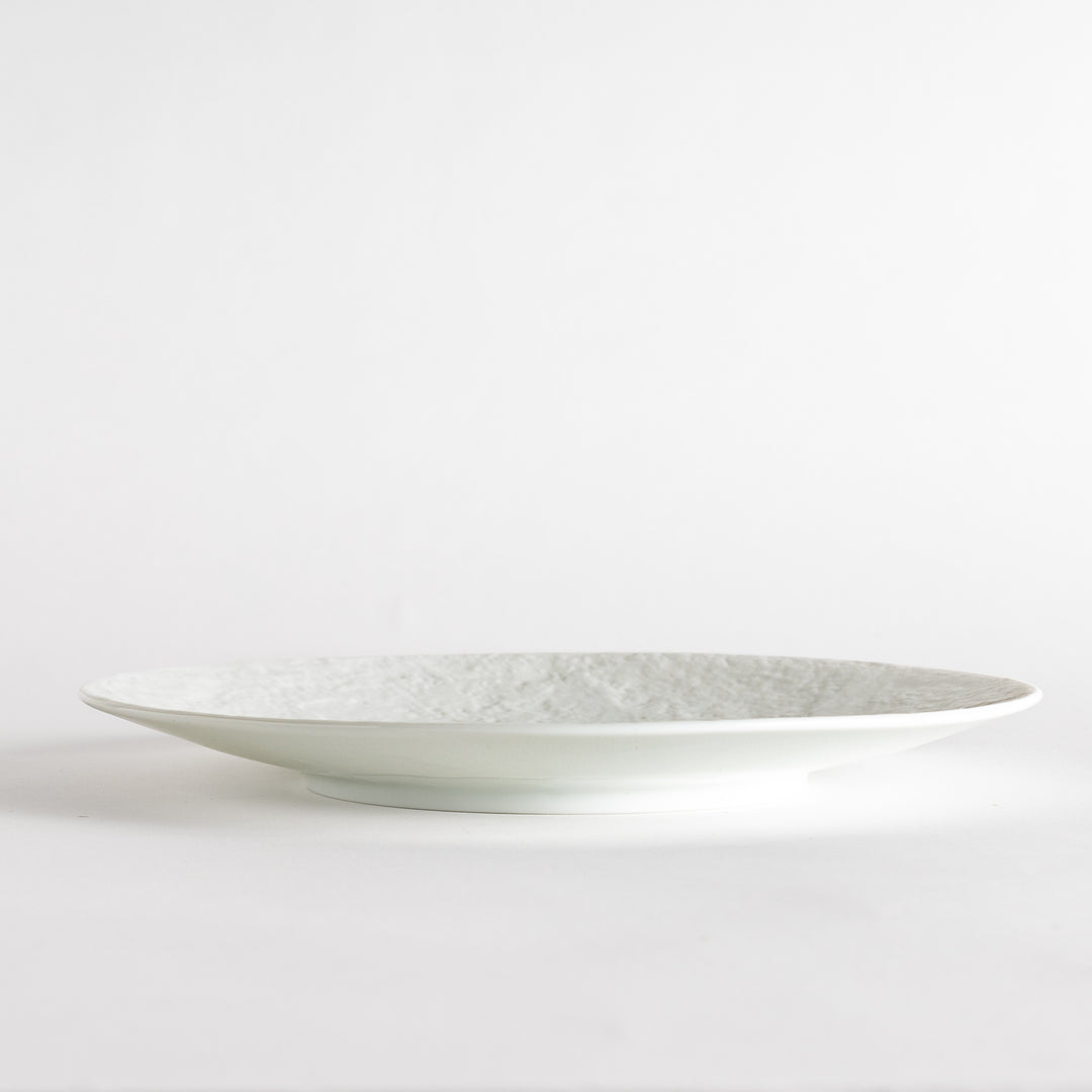 A white luncheon plate featuring a slightly irregular, organic texture and shape, providing a minimalist and natural look.