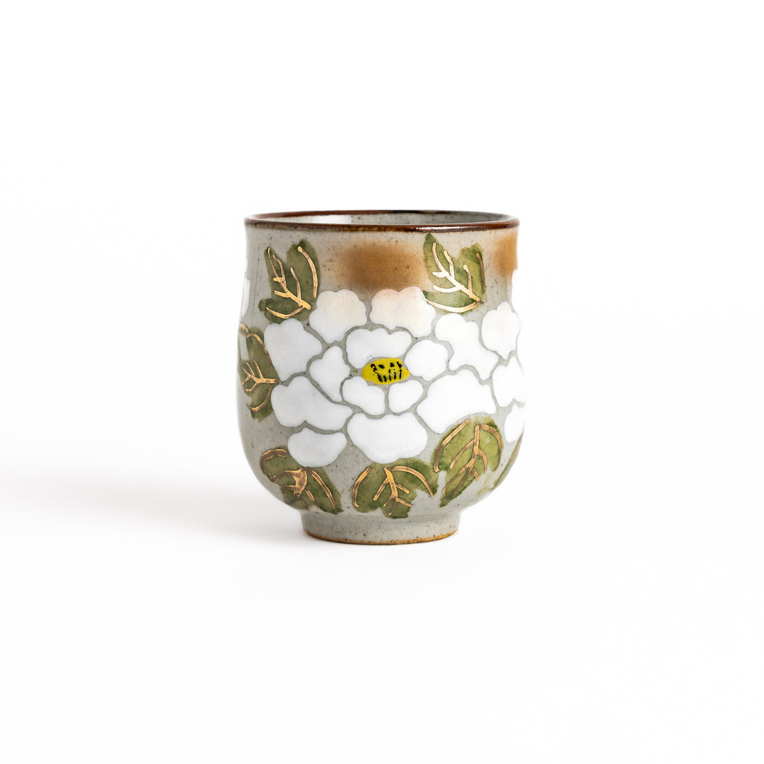 Ceramic teacup with a delicate white flower design and green leaves, perfect for enjoying a peaceful moment with tea.