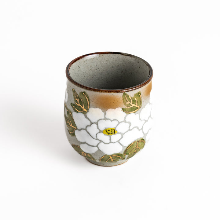 Ceramic teacup with a delicate white flower design and green leaves, perfect for enjoying a peaceful moment with tea.