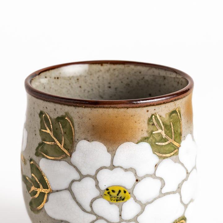 Ceramic teacup with a delicate white flower design and green leaves, perfect for enjoying a peaceful moment with tea.