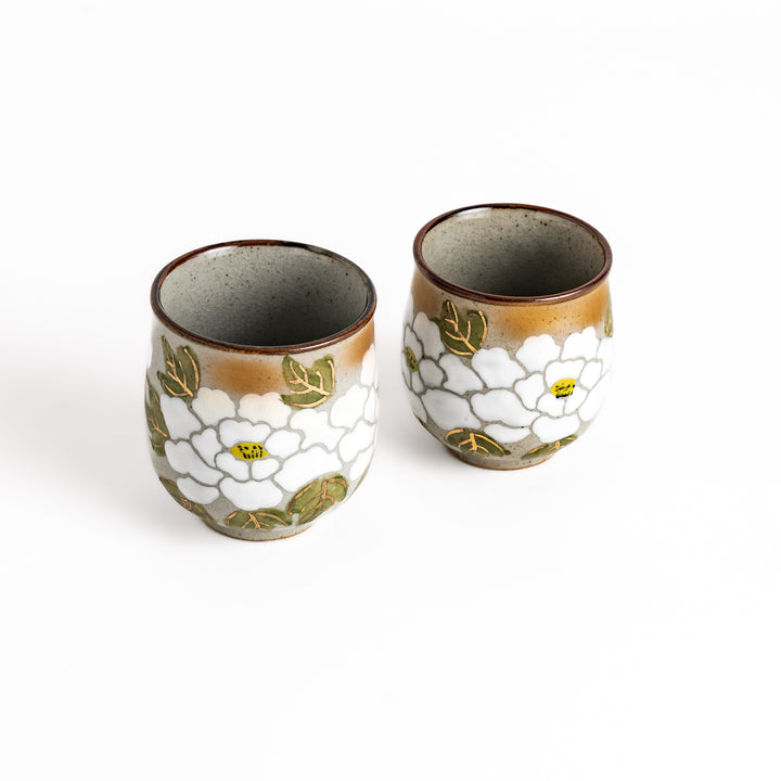 Two ceramic teacups with a beautiful white flower design and green leaves, perfect for enjoying tea for two.