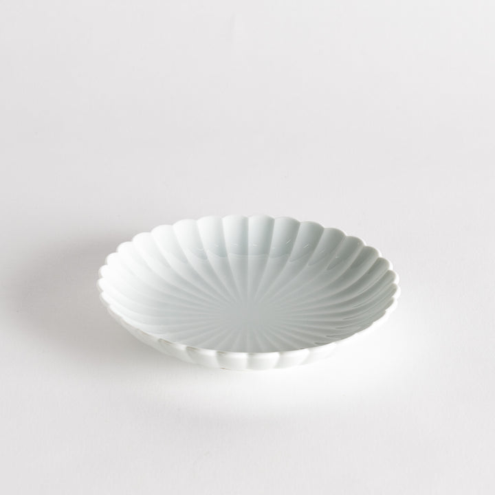 A simple white ceramic plate with a scalloped edge and a clean, minimalist design.