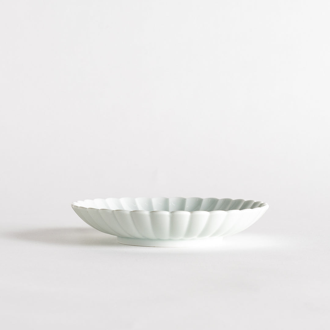 A simple white ceramic plate with a scalloped edge and a clean, minimalist design.