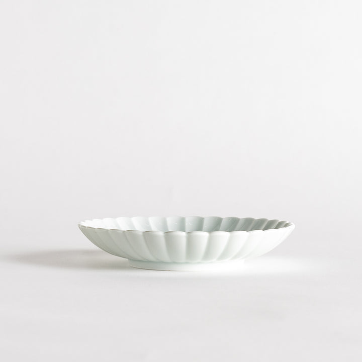 A simple white ceramic plate with a scalloped edge and a clean, minimalist design.