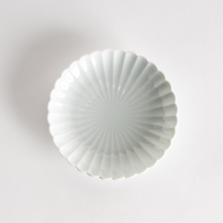 A simple white ceramic plate with a scalloped edge and a clean, minimalist design.