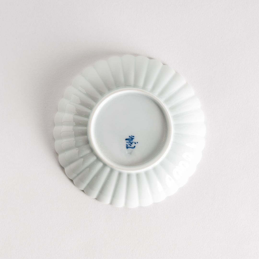 A simple white ceramic plate with a scalloped edge and a clean, minimalist design.