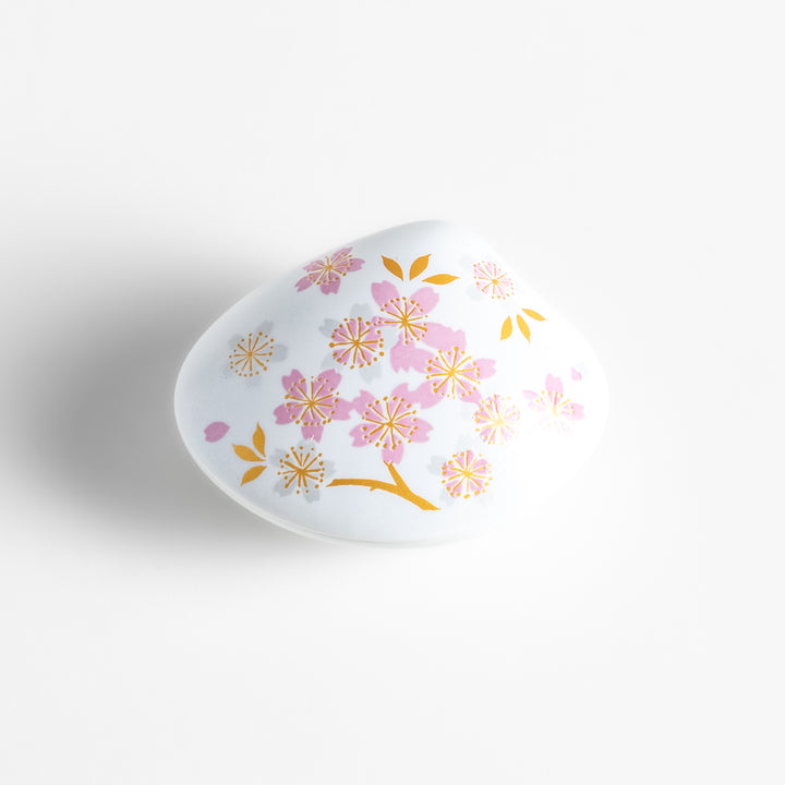 White ceramic incense holder shaped like a seashell, adorned with delicate pink and gold cherry blossoms, featuring a sakura-shaped holder for a refined touch.