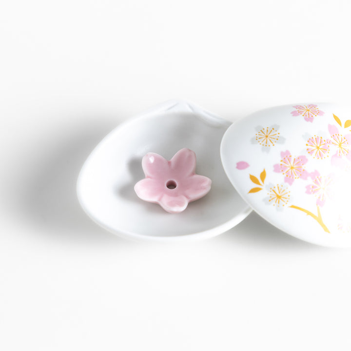 White ceramic incense holder shaped like a seashell, adorned with delicate pink and gold cherry blossoms, featuring a sakura-shaped holder for a refined touch.