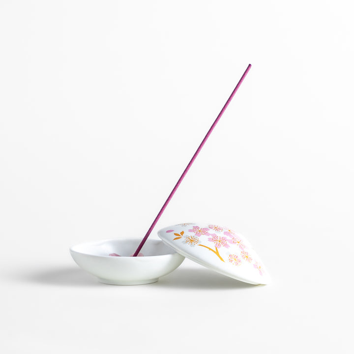 White ceramic incense holder shaped like a seashell, adorned with delicate pink and gold cherry blossoms, featuring a sakura-shaped holder for a refined touch.