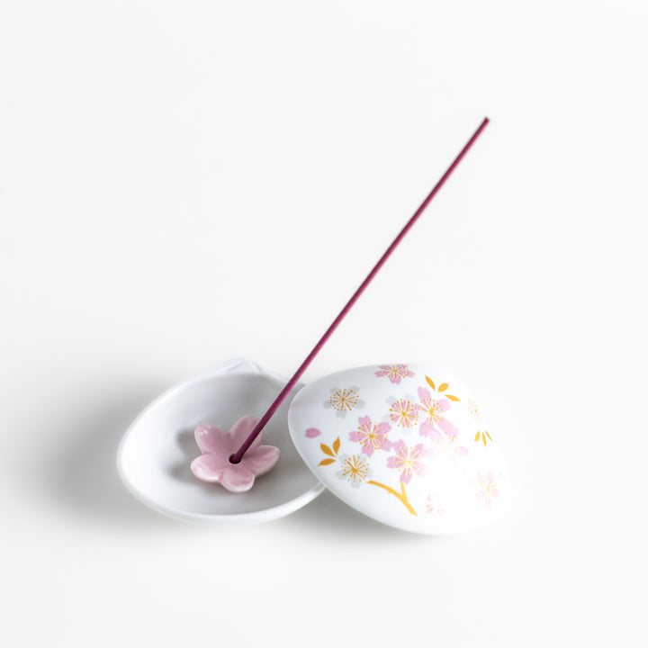 White ceramic incense holder shaped like a seashell, adorned with delicate pink and gold cherry blossoms, featuring a sakura-shaped holder for a refined touch.