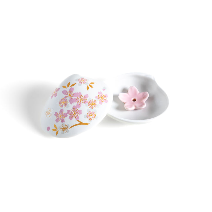 White ceramic incense holder shaped like a seashell, adorned with delicate pink and gold cherry blossoms, featuring a sakura-shaped holder for a refined touch.