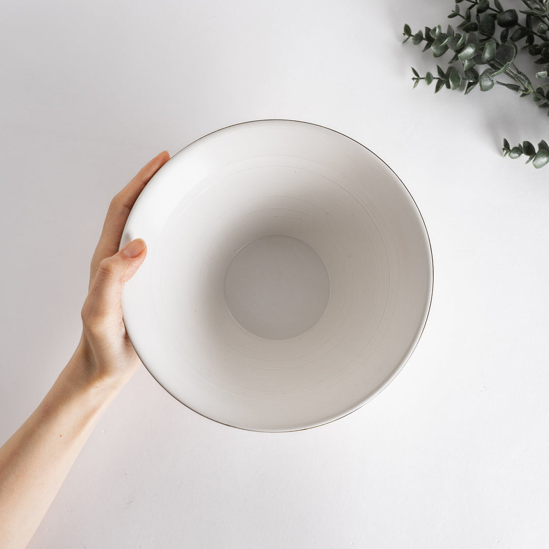 Hand holding the white spiral flared ramen bowl from above, highlighting its elegant design against a light background.