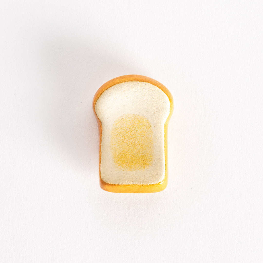 A ceramic chopsticks rest shaped like a slice of toasted bread, featuring a golden-brown edge and soft white center.