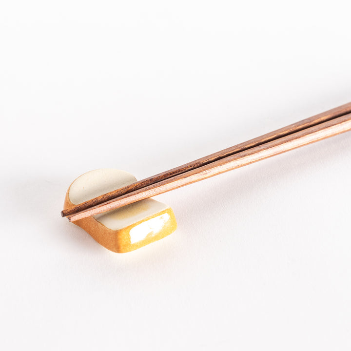 A close-up of the toast-shaped chopsticks rest with chopsticks placed across its surface.