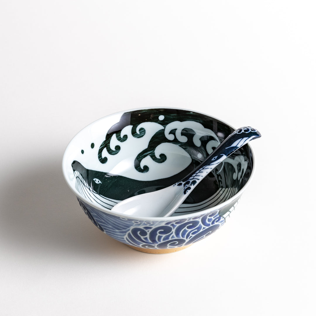 A white ramen bowl with a whale and wave design, accompanied by a matching spoon.