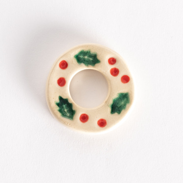 A ceramic chopstick rest shaped like a wreath, decorated with green holly leaves and red berries on a white base.