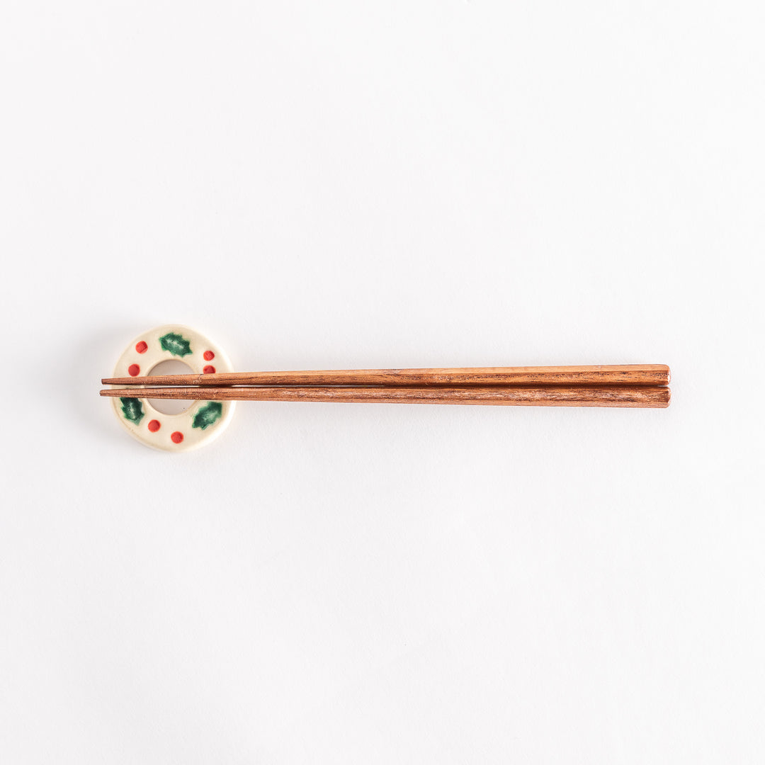 A wide view of the white wreath-shaped chopstick rest holding chopsticks, emphasizing the intricate holly and berry pattern.