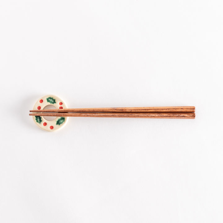 A wide view of the white wreath-shaped chopstick rest holding chopsticks, emphasizing the intricate holly and berry pattern.