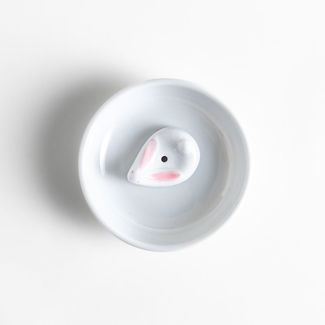 White ceramic incense holder set featuring a round dish and a rabbit-shaped holder with pink accents, designed to catch ash neatly while adding a charming touch.