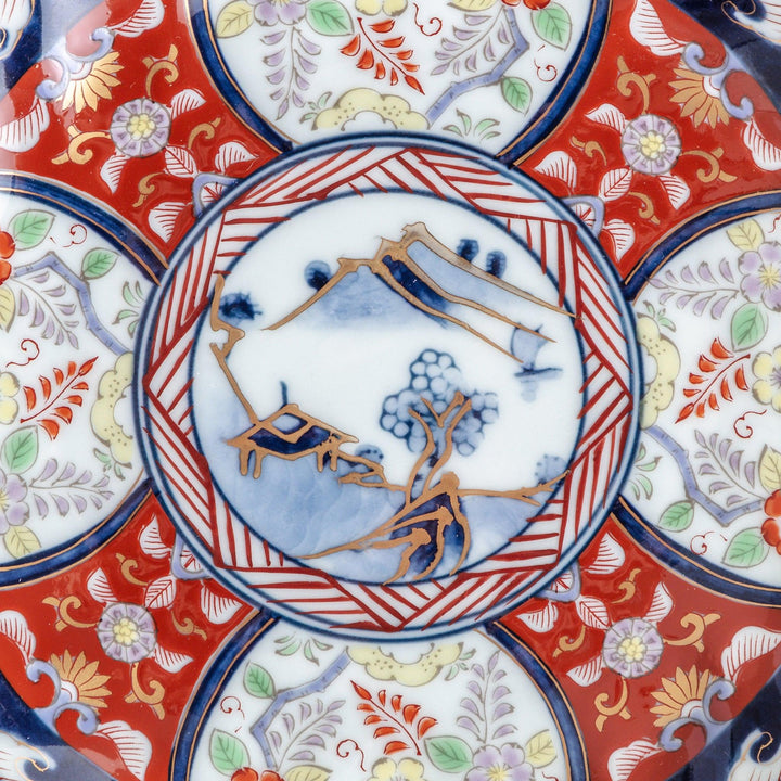 A smaller scalloped porcelain bowl with Imari-style decoration, showcasing a central landscape and vibrant red and blue motifs around the rim.