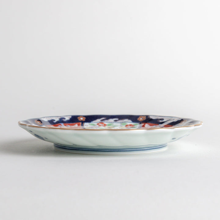 A smaller scalloped porcelain bowl with Imari-style decoration, showcasing a central landscape and vibrant red and blue motifs around the rim.