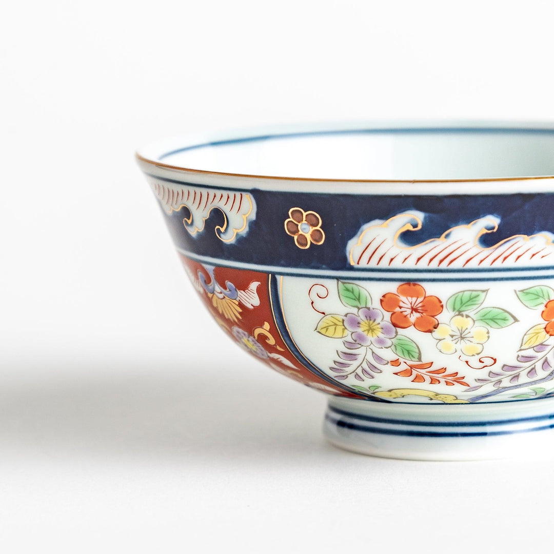 A porcelain bowl adorned with traditional Japanese motifs, including floral and geometric designs in blue, red, and green with gold accents.