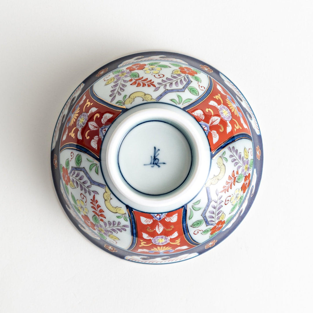 A porcelain bowl adorned with traditional Japanese motifs, including floral and geometric designs in blue, red, and green with gold accents.