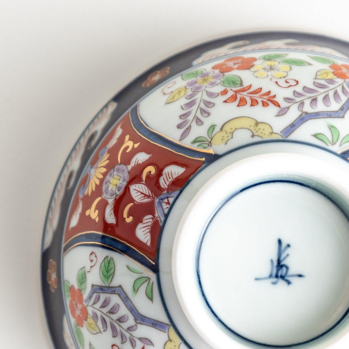 A porcelain bowl adorned with traditional Japanese motifs, including floral and geometric designs in blue, red, and green with gold accents.