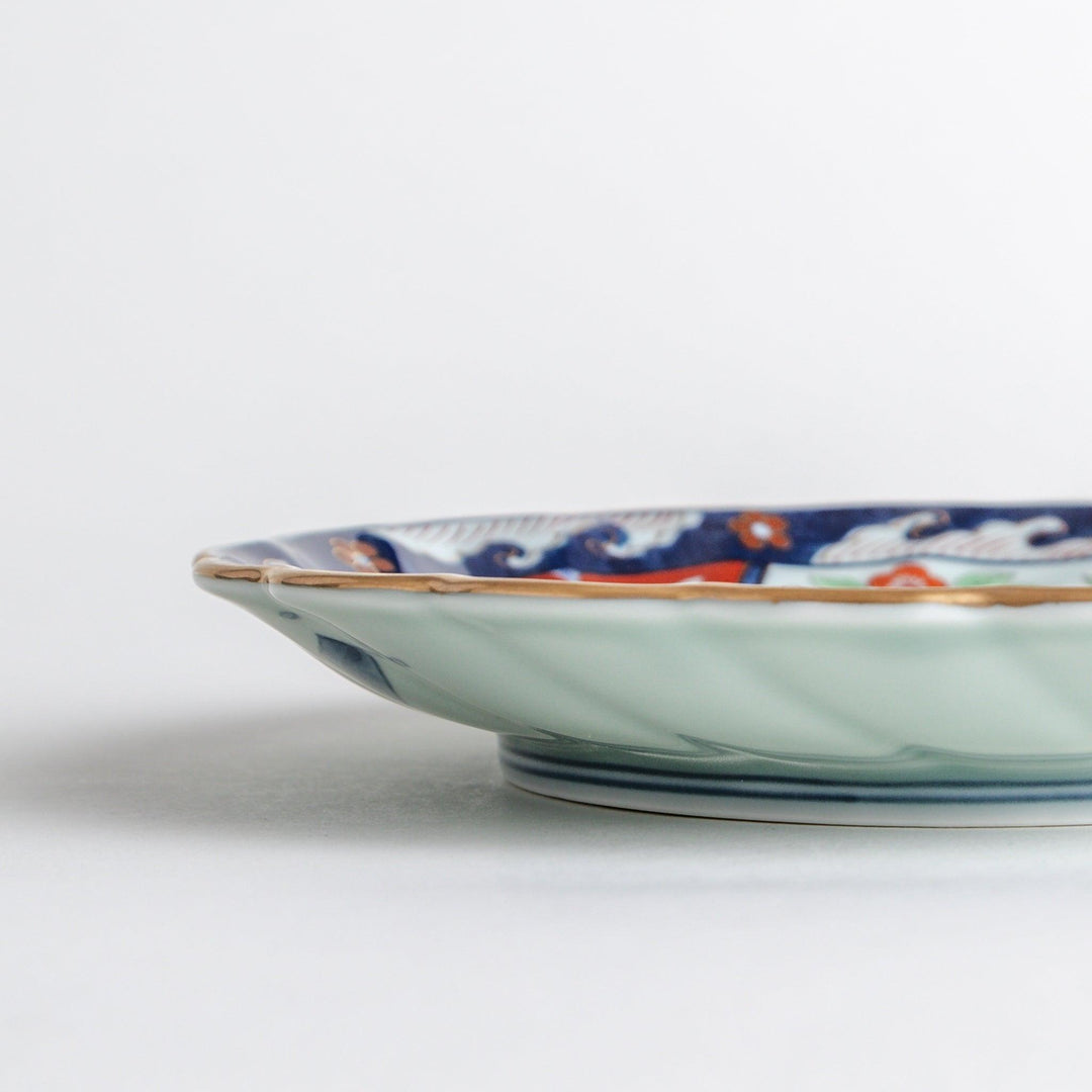 A scalloped porcelain bowl featuring an intricate Imari-style design with alternating red and blue patterns and a central landscape scene.