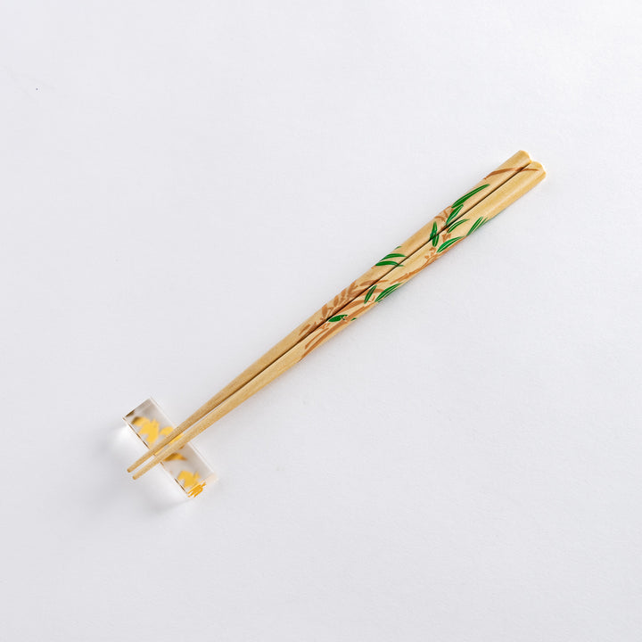 Close-up of chopsticks decorated with wisteria flowers in purple and green bamboo leaves. Displayed with a clear stand.