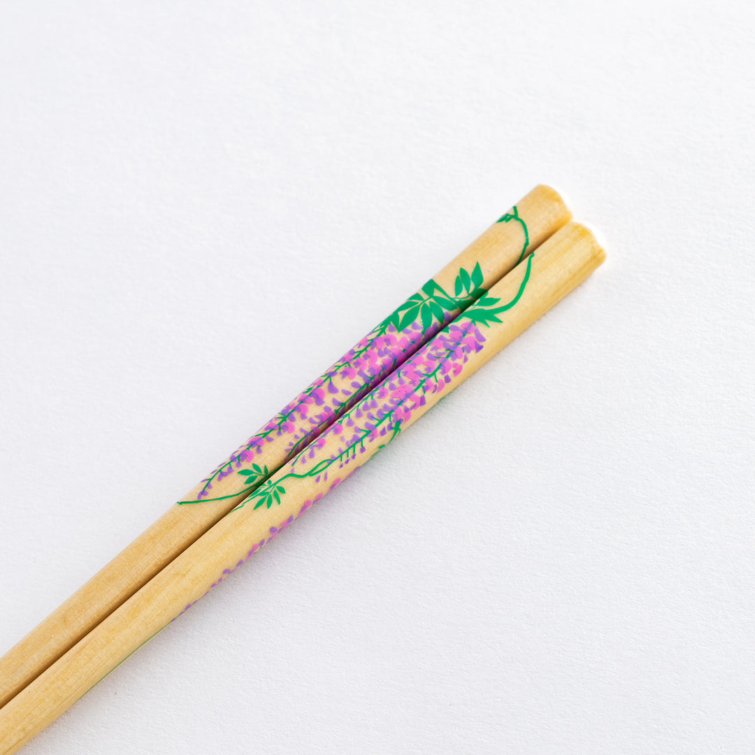 Close-up of chopsticks with wisteria and bamboo design on one side, resting on a holder.