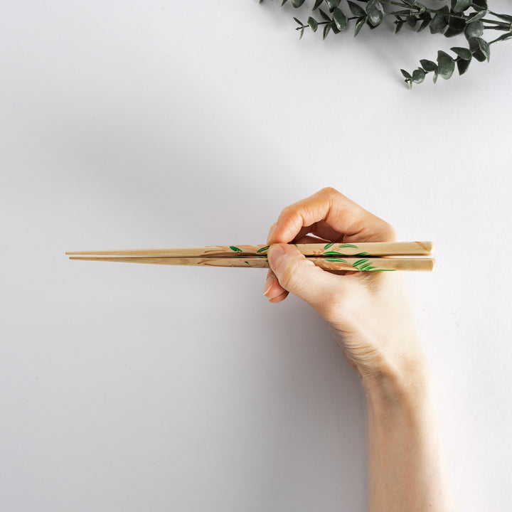 Hand holding chopsticks with wisteria flower design, showcasing their size and intricate detail.