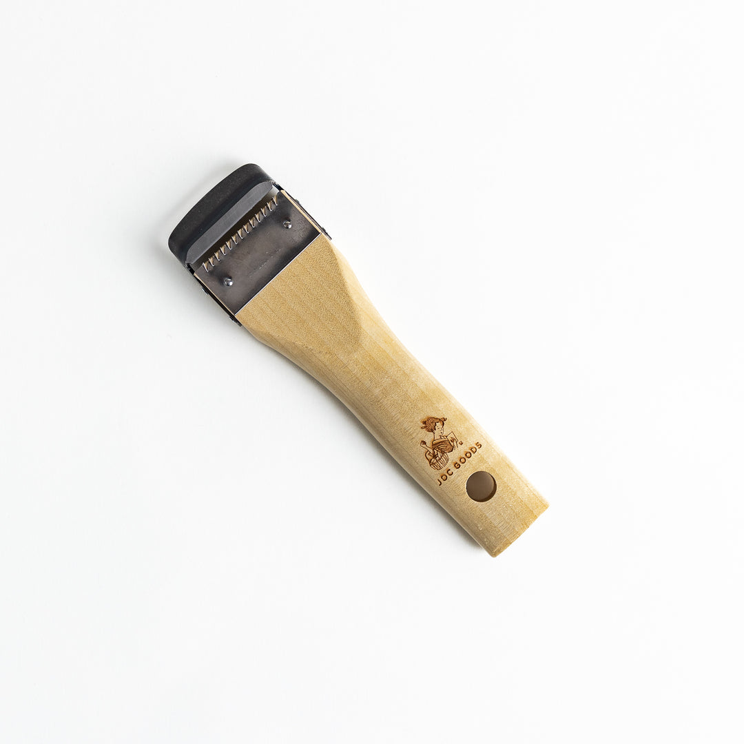 A Wood Handle Julienne Peeler, a piece of kitchenware in use to create thin vegetable strips from a carrot, perfect for salads and garnishes.