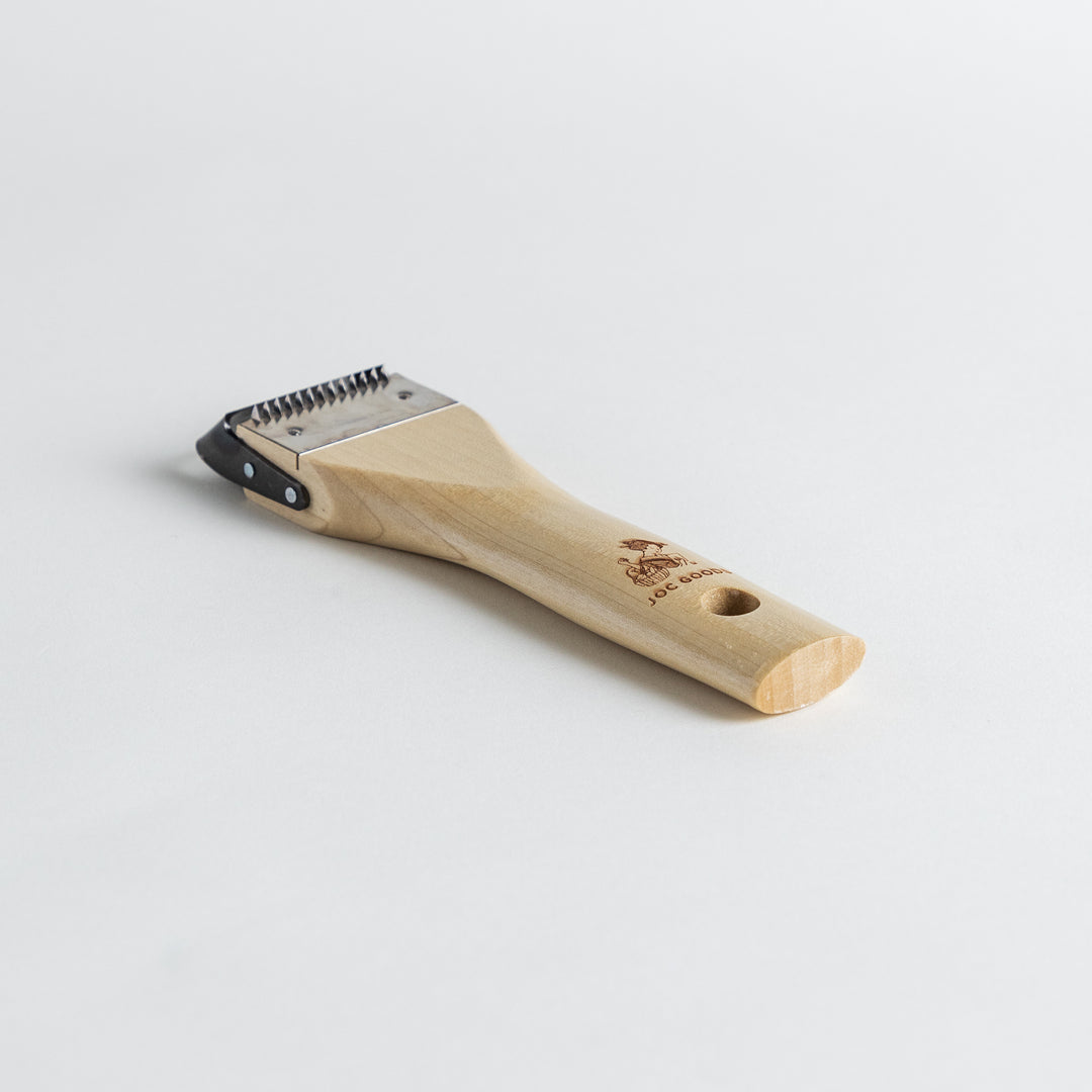 A Wood Handle Julienne Peeler, a piece of kitchenware in use to create thin vegetable strips from a carrot, perfect for salads and garnishes.