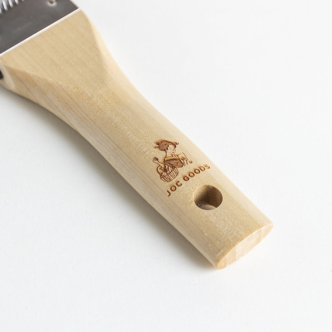 A Wood Handle Julienne Peeler, a piece of kitchenware in use to create thin vegetable strips from a carrot, perfect for salads and garnishes.