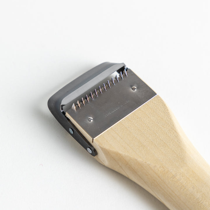 A Wood Handle Julienne Peeler, a piece of kitchenware in use to create thin vegetable strips from a carrot, perfect for salads and garnishes.