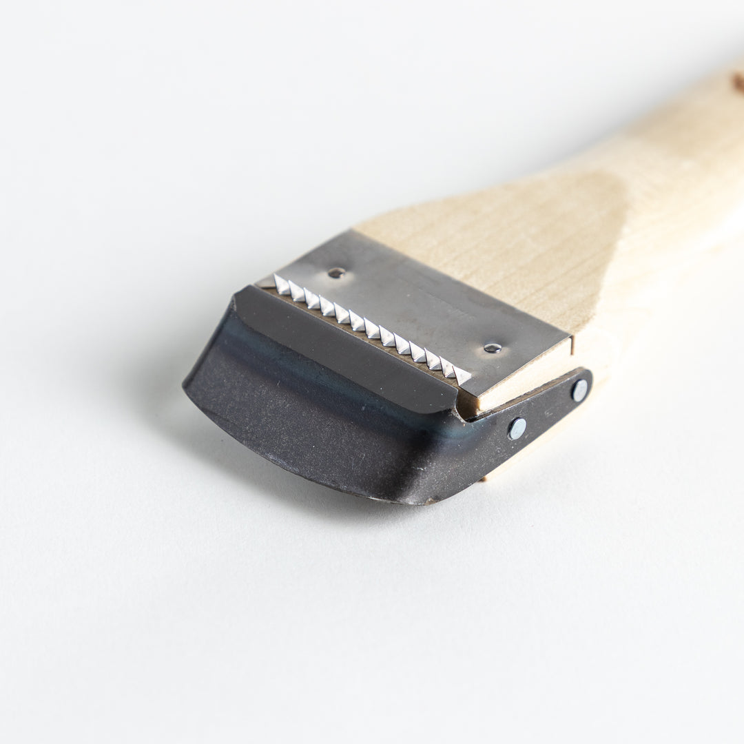 A Wood Handle Julienne Peeler, a piece of kitchenware in use to create thin vegetable strips from a carrot, perfect for salads and garnishes.