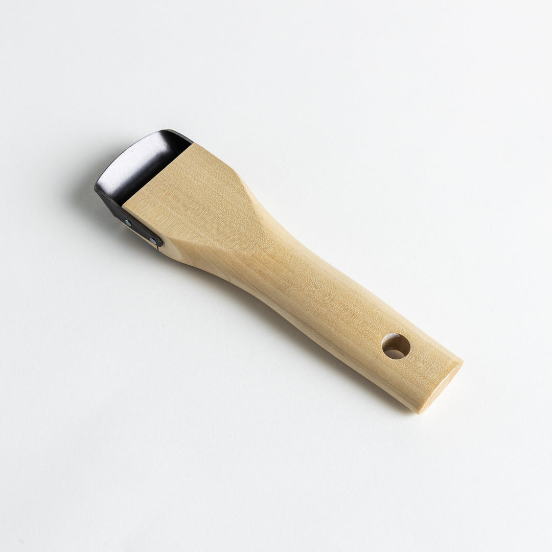 A Wood Handle Julienne Peeler, a piece of kitchenware in use to create thin vegetable strips from a carrot, perfect for salads and garnishes.