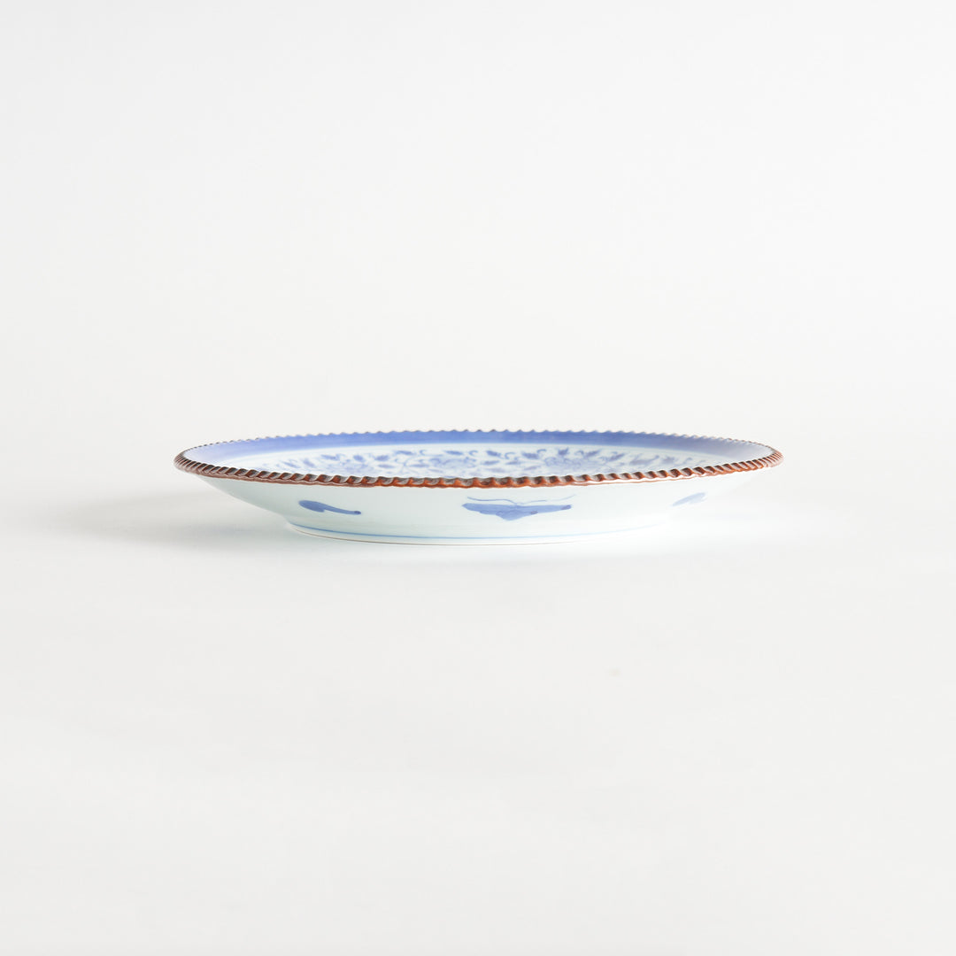 A ceramic plate with an intricate blue floral design centered around a bold circular pattern, framed by a copper-colored textured rim.