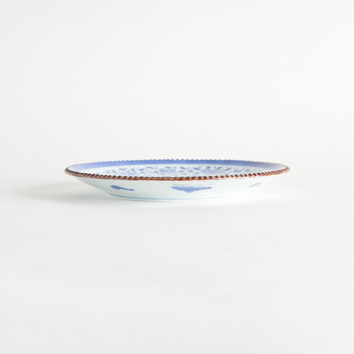 A ceramic plate with an intricate blue floral design centered around a bold circular pattern, framed by a copper-colored textured rim.