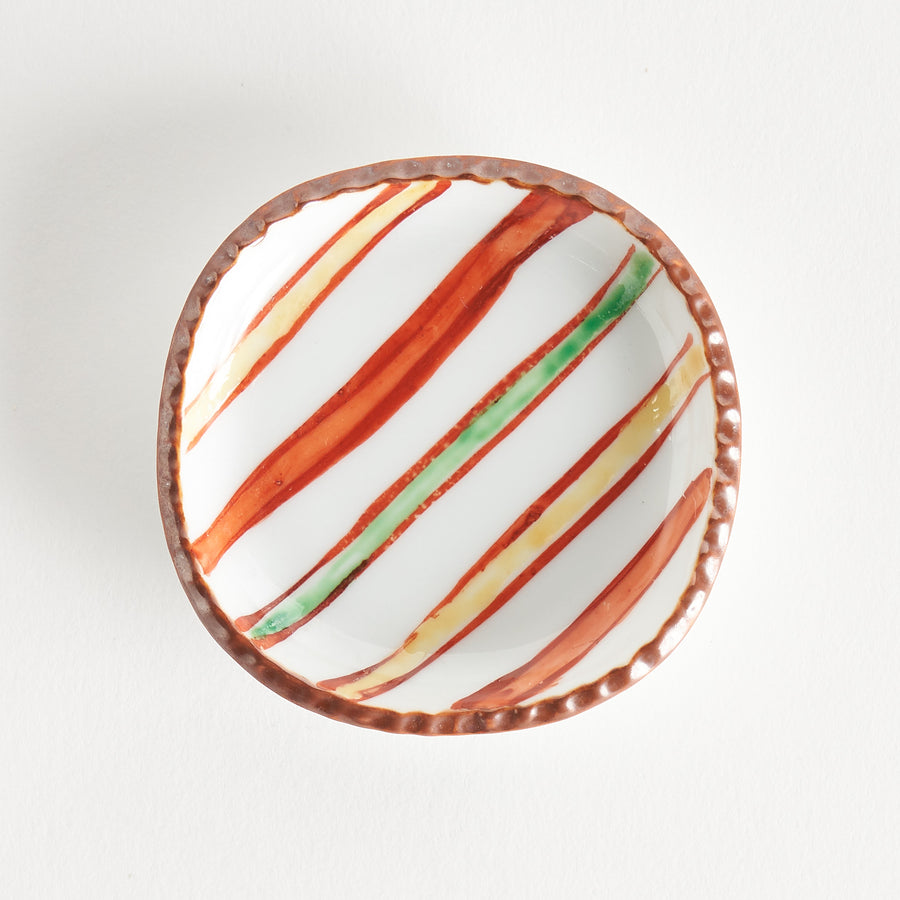 Top view of a sauce dish with colorful stripes of red, green, and yellow against a white background, featuring a textured rim.