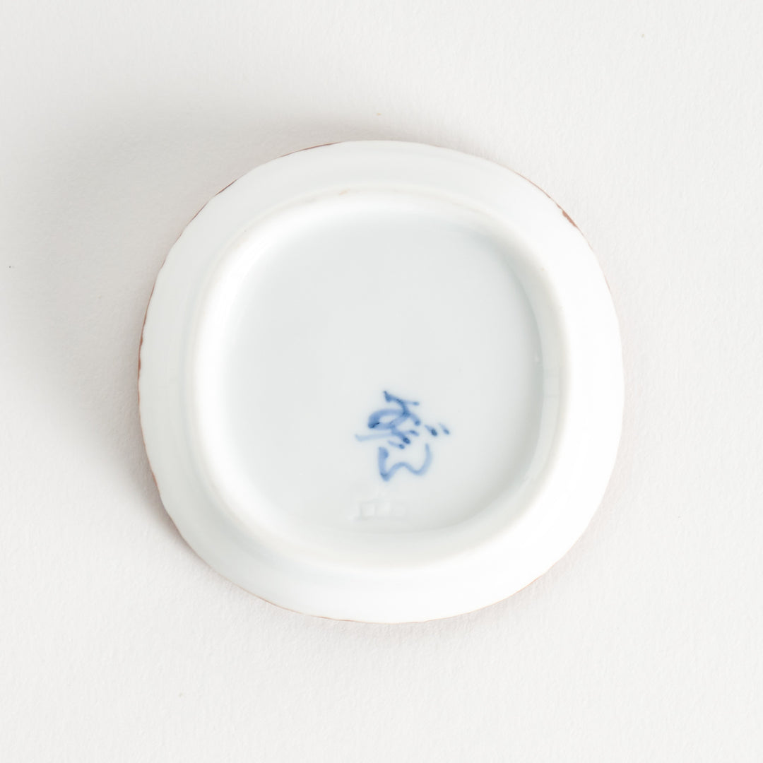 Bottom view of the sauce dish, displaying the manufacturer's mark in blue ink on a smooth surface.