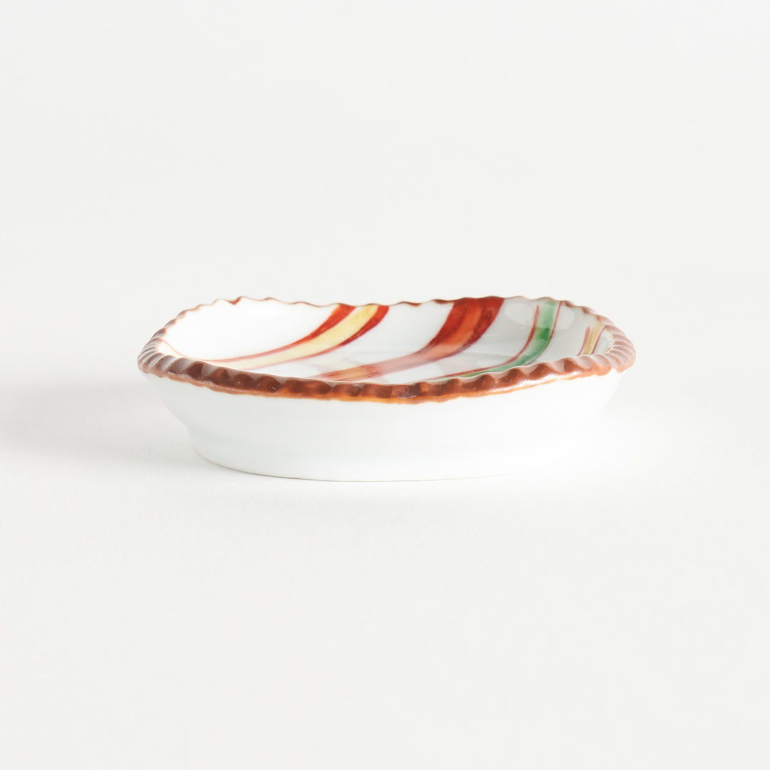 A tilted view of a colorful striped sauce dish, emphasizing the vibrant lines and textured edge.