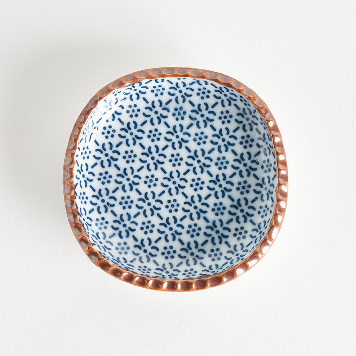 A round plate featuring a blue dotted geometric pattern with a textured brown rim.