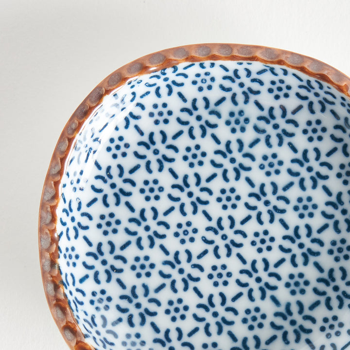 A round plate featuring a blue dotted geometric pattern with a textured brown rim.