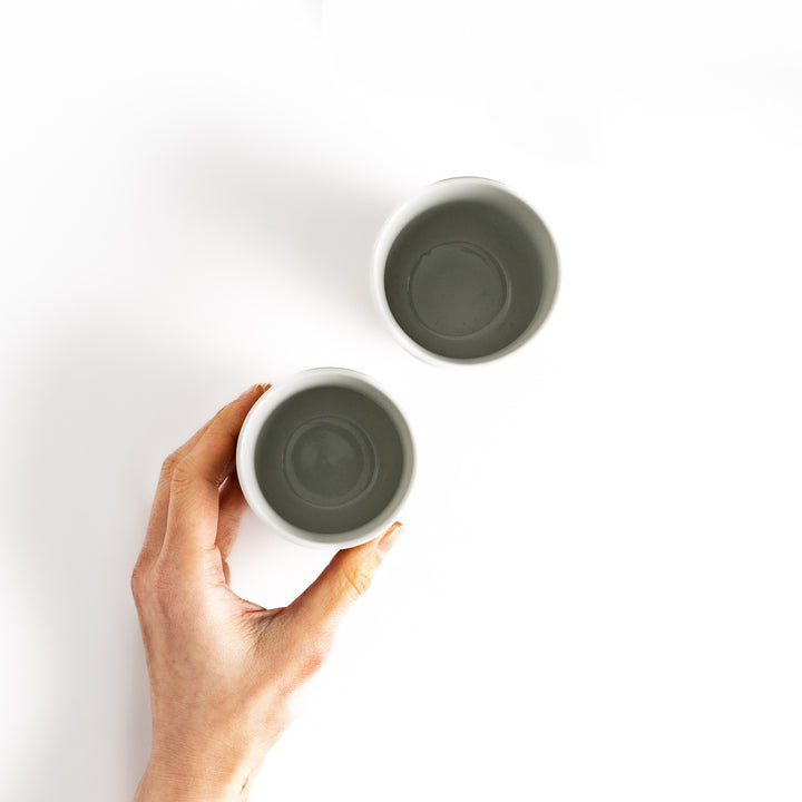 Hand holding a small, simple teacup with a white glaze, next to another identical teacup, viewed from above.